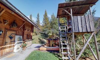 A rustic wooden cabin with a small garden. Next to the cabin, there is a lookout tower with a wooden staircase.