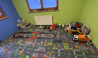 A colorful playroom with a prominent vehicle carpet. Toy cars and building blocks are scattered on the floor.