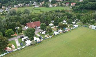 An aerial shot of a campsite next to a football field. In the background, residential houses and green landscapes are visible.