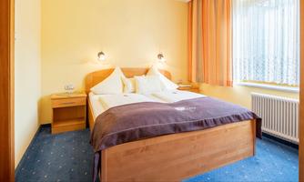A cozy room with a double bed and bright walls. There is a desk and plenty of daylight through the windows.