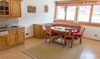 A bright kitchen with wooden cabinets and a round table. Comfortable seating and large windows create an inviting atmosphere.