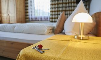 A cozy room with a bed and a modern lamp on a yellow table. Keys are lying on the table.