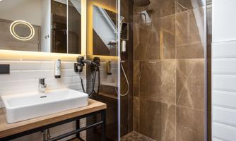 A modern bathroom with a spacious shower and elegant lighting. The furnishings consist of wood and tiles in warm colors.