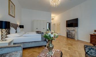 An elegant bedroom with a large bed and modern furniture. A beautiful chandelier hangs from the ceiling and a flower arrangement is on a table.