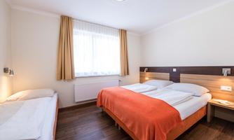 A bright room with two double beds and one single bed. The windows are fitted with curtains, and the floor is made of wood.
