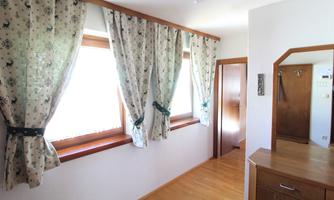 A bright hallway with wooden flooring and large windows. The windows are adorned with decorative curtains.