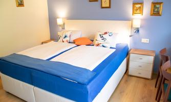 A cozy bedroom with a large double bed and a blue wall. There are two nightstands with lamps and decorative pictures.