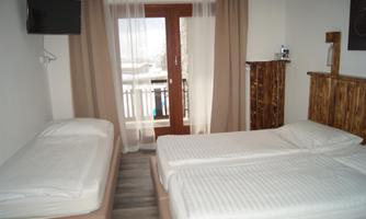 A simple room with two beds and a single bed. There is a balcony and a television on the wall.