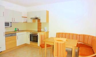 A modern kitchen with wooden cabinets and appliances. A dining area with a table and a cozy bench is also available.