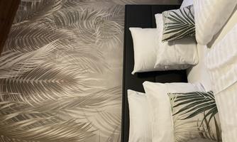 A cozy bedroom with a modern bed and many pillows. The wall is decorated with a beautiful palm leaf pattern.