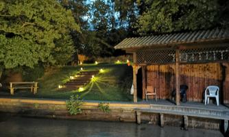 A quiet water area with a wooden terrace and a small house. In the background, illuminated steps lead through the garden.