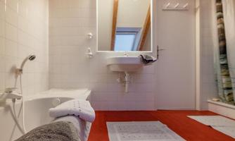 A modern bathroom with a bathtub and a bright mirror. The floor is covered with red carpets, and the walls are tiled in white.