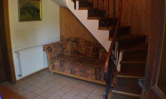 A cozy entrance area with a sofa and a curved staircase. The walls are clad in wood and there is a heater.