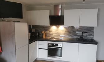 A modern kitchen with white cabinets and a gray tiled backsplash. It is equipped with a stove, an oven, and a sink.