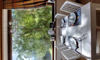 A bright dining area with a white table and chairs. Through the large window, you can see green foliage and a beautiful view of nature.
