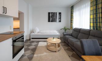 A modern living room with a gray couch and a round table. Bright windows with yellow curtains create a friendly atmosphere.