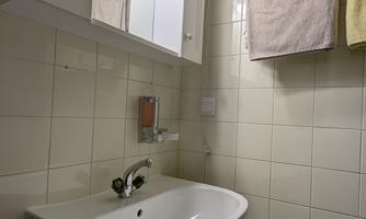 A small bathroom with a sink and a mirror. Towels are hanging on the wall, and a stool is standing next to it.