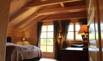 A cozy room with wooden paneling and a large window. The room is furnished with a bed, a desk, and a lamp.
