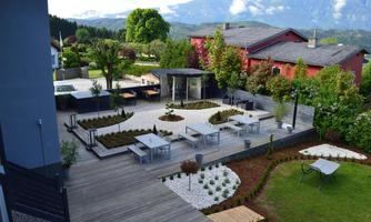 A modern garden with elegant seating areas and beautifully designed flower beds. In the background, green hills and a clear sky are visible.