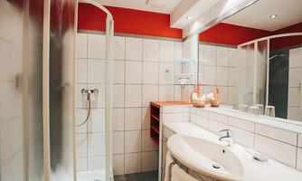A modern bathroom with a shower, a sink, and bright tiles. The walls are red and there is pleasant lighting.