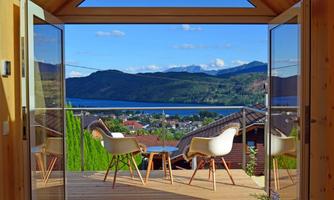 A modern room with glass sliding doors that offers a view of a picturesque landscape. In the foreground, two elegant chairs are positioned on a wooden terrace.