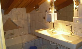 A small bathroom with sloping walls and a wooden ceiling. It features a double sink, a bathtub, and large mirrors.