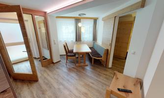 A modern living space with a wood-colored table and chairs. The room is bright and inviting, with large windows and a cozy atmosphere.