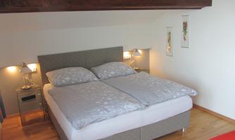 A cozy bedroom with a large double bed and modern nightstands. The walls are light, and there is a pleasant atmosphere with warm lighting.