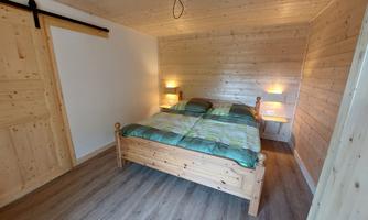 A cozy bedroom with a wooden bed and two nightstands. The walls are made of wood, and there is soft lighting.