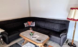 A modern living room with a dark gray sofa and a coffee table. A floor lamp and some decorative elements are also visible.
