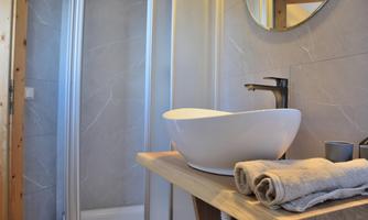 A modern bathroom with an elegant sink and a large mirror. Soft towels are placed on a wooden shelf next to a shower.