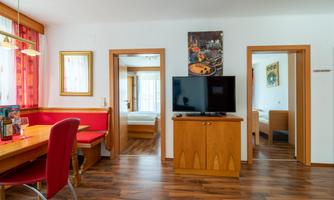 A modern living room with a television and a dining area. Two doors lead to bedrooms and the walls are light and welcoming.
