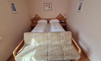 A simple hotel room with two single beds and a cozy sofa. The walls are painted in soft colors, and there are some pictures on the walls.