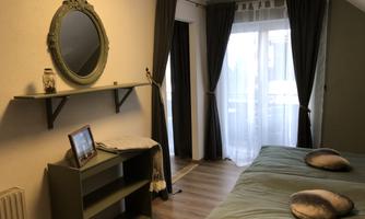 A cozy bedroom with two beds and a large mirror. Curtains and a shelf give the room an inviting look.