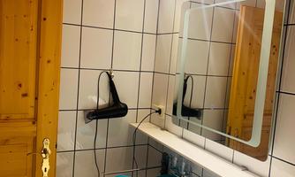 A modern bathroom with tiled walls and a round sink. On the shelf lie turquoise towels and a hairdryer hangs on the wall.