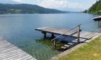 A tranquil lake with a wooden pier and a wide view of the surrounding mountains. The water's surface is clear and reflects the sky.