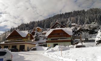 A winter village with snow-covered houses and pine trees. The sky is partly cloudy and the landscape is picturesque.
