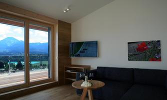 A modern living room with a comfortable sofa and a coffee table. Large windows offer a view of mountains and a lake.
