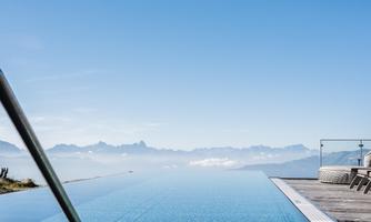 An infinity pool with a breathtaking view of the mountains. The sky is clear and blue.