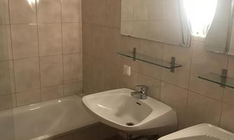 A modern bathroom with a bathtub and two sinks. The walls are tiled, and large mirrors reflect the light.