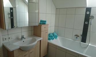 A modern bathroom with a bathtub and a sink. Blue towels are neatly placed on the bathtub, and there are large mirrors on the walls.