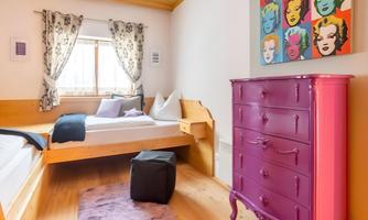 A bright room with a modern design and a large window. A purple dresser and colorful artworks on the wall give the space a stylish accent.