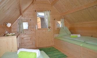 A cozy wooden room with two single beds and a bright wood paneling. The shutters and curtains in fresh colors give the room an inviting atmosphere.