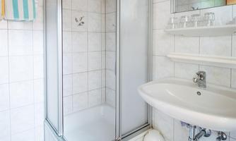 A bathroom with a shower cabin and a sink. The walls are lightly tiled, and there is a wooden ceiling.