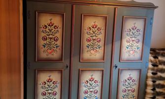 A beautiful, historic wardrobe with colorful floral patterns. The wardrobe has three doors and is made of wood.