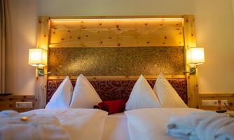 A cozy bedroom with a wooden headboard and soft lighting. The beds are decorated with white pillows and a red blanket.