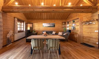 A cozy room with wooden walls and a large dining table. There are comfortable sofas and a relaxed atmosphere.