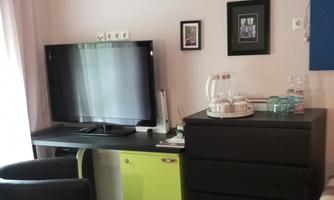 TV on a desk, next to a dresser with tea station and a small refrigerator; an armchair in front.