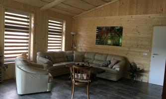 A cozy living room with wooden paneling and large windows. There is a comfortable couch, a table, and a modern lamp.