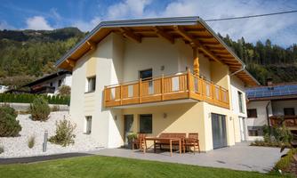 A modern house with a balcony and a beautiful terrace. Surrounded by a well-maintained lawn and mountains in the background.